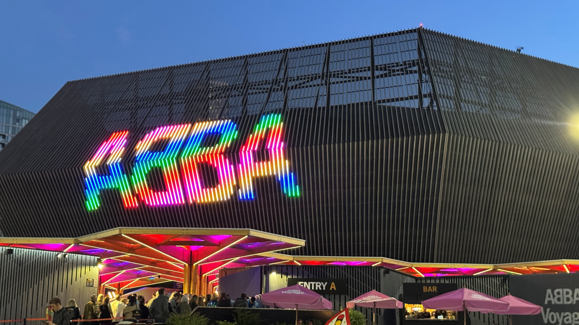 A photo of Abba Arena in Stratford at night with a multicoloured sign spelling out Abba as people walk into the venue 