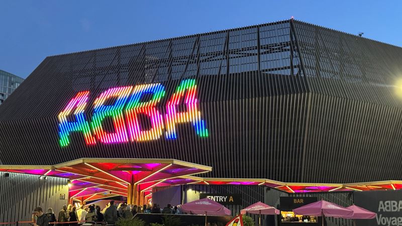 Abba Arena. Credit: Jou Jou Travels. Image courtesy of Jou Jou Travels. A photo of Abba Arena in Stratford at night with a multicoloured sign spelling out Abba as people walk into the venue