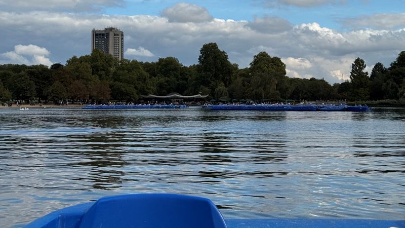Hyde Park boating. Credit: Jou Jou Travels. Image courtesy of Jou Jou Travels. A photo of the Boating Lake in Hyde Park with trees and blue sky in the background with boats on the lake and the boat in the foreground