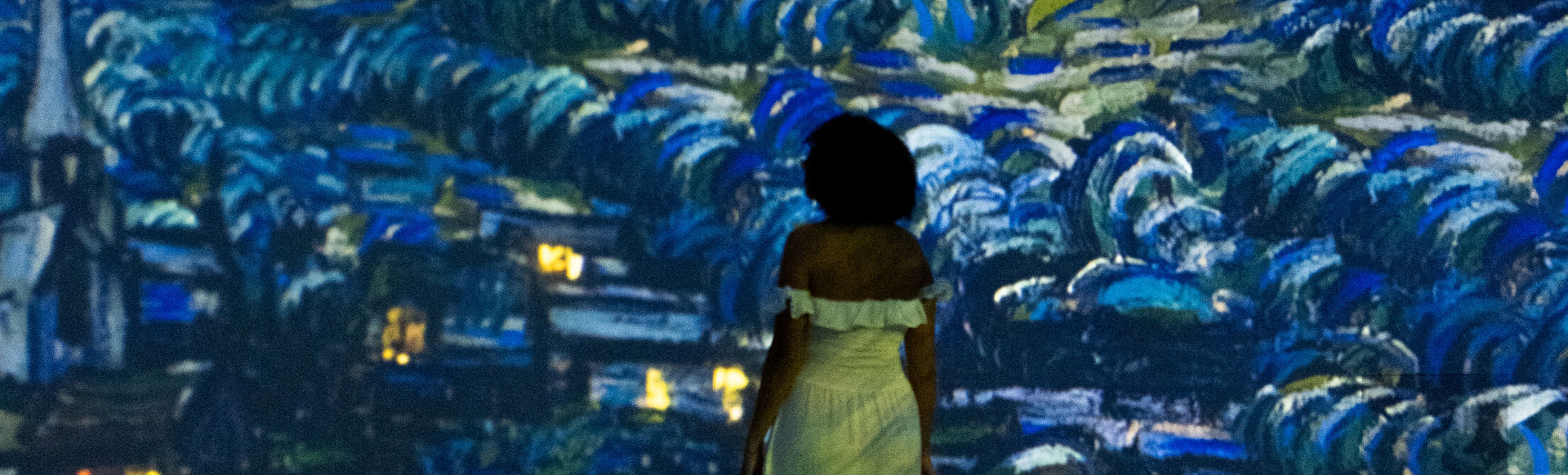 A photo of Jou Jou Travels travel influencer from behind stood in front of one of the giant interactive screens projecting Van Gogh Starry Night