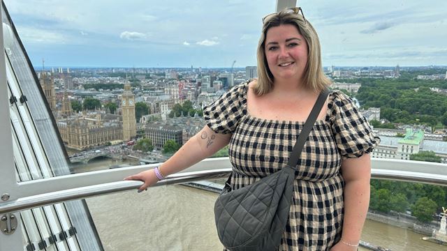 Person standing inside a London Eye capsule with the Big Ben, the Palace of Westminster and the river Thames visible in the background.