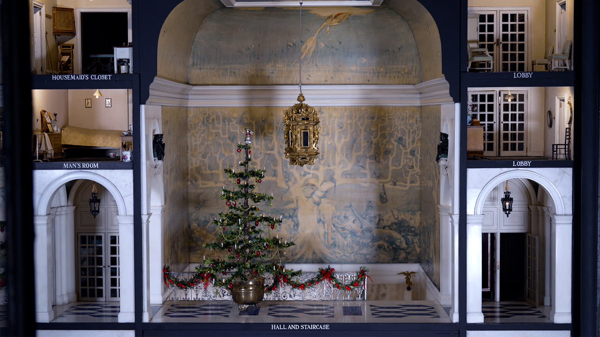 See the intricate designs at Queen Mary's Doll House at Windsor Castle with Christmas decorations. © Royal Collection Enterprises Limited 2025 | Royal Collection Trust The grand Hall and staircase in Queen Mary's dollhouse decorated with a Christmas tree and festive garlands on the staircase.