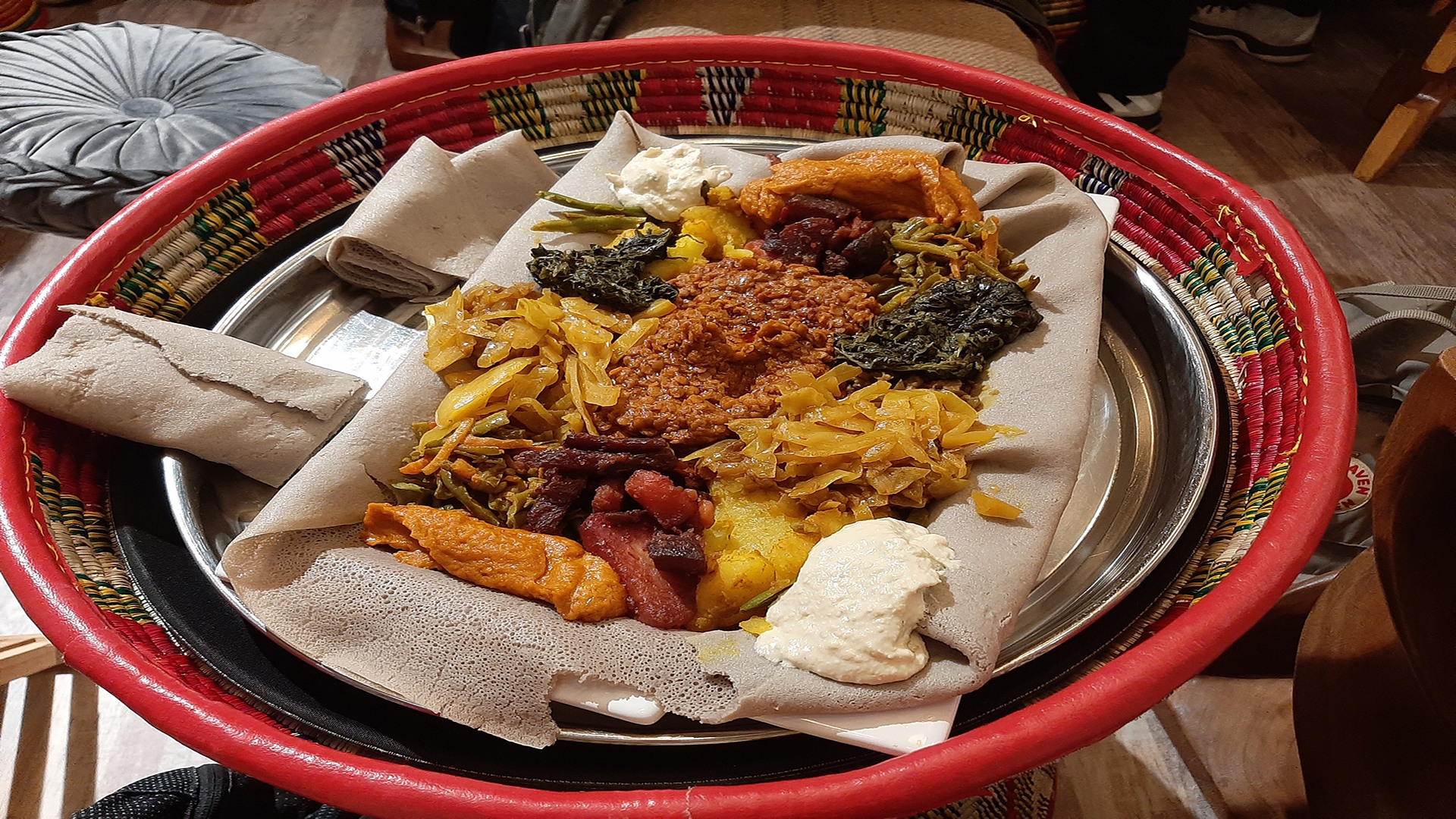 A large plate with a flat injera bread which has various colourful toppings and sauces on top.