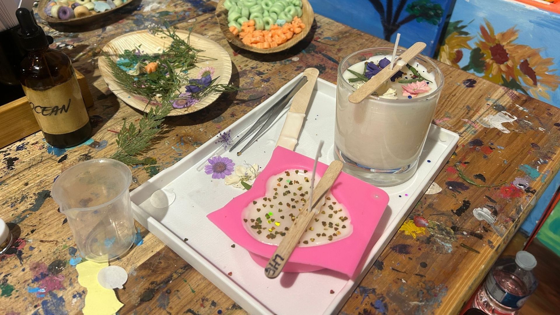 A table with a tray of materials to make candles on top, including wooden sticks, a candle holder and decorations.