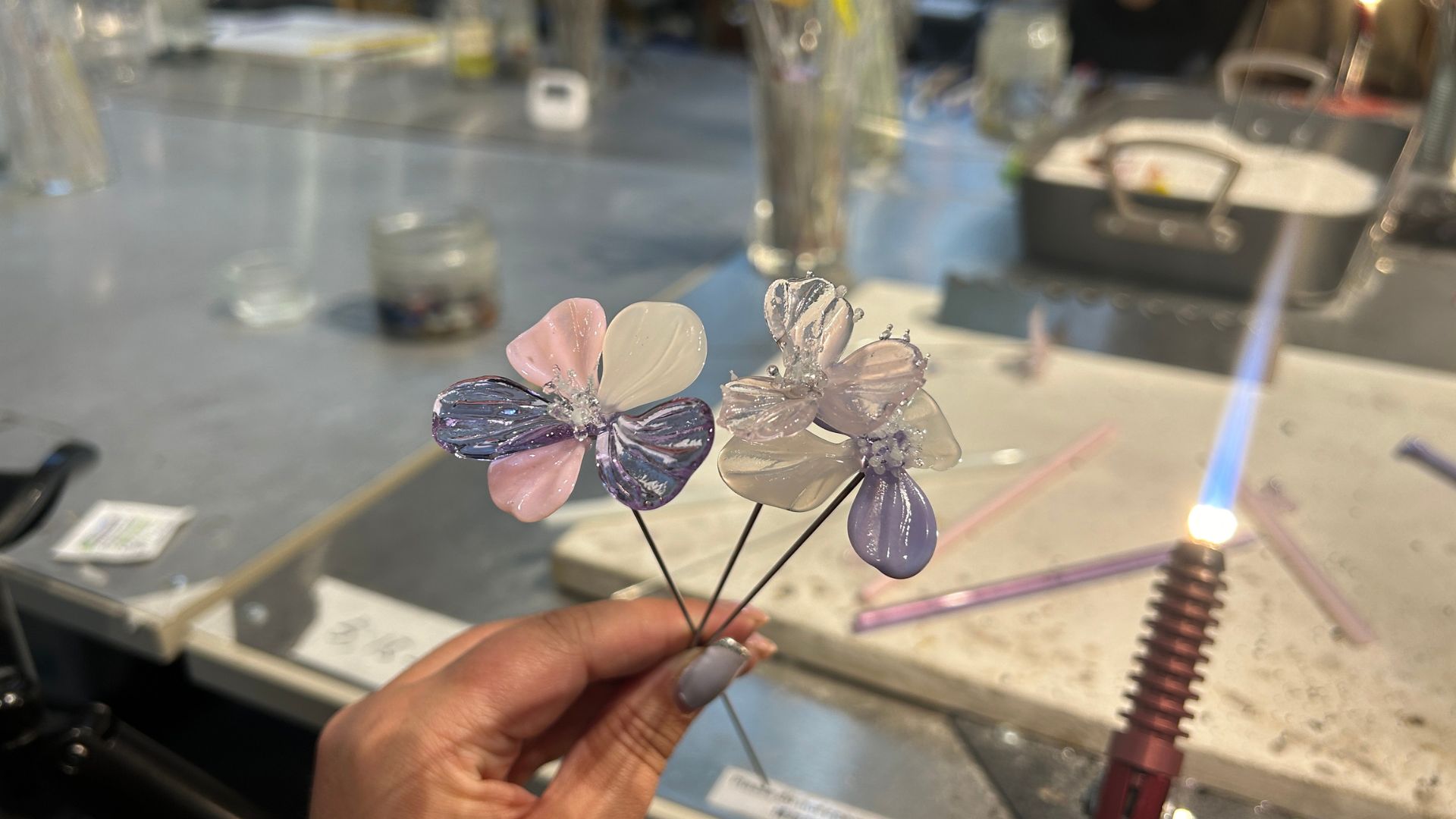 A woman holds two glass flowers that she has created during a lampworking glass workshop at SONG Art & Craft.