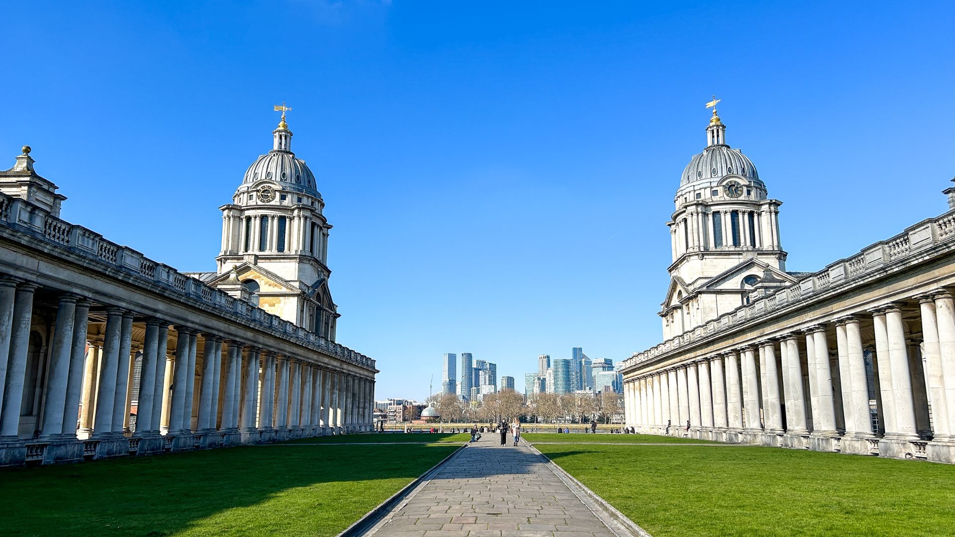 a picture taken from the middle of Old Royal Naval College, with blue skies and a glimpse of the London skyline in the background