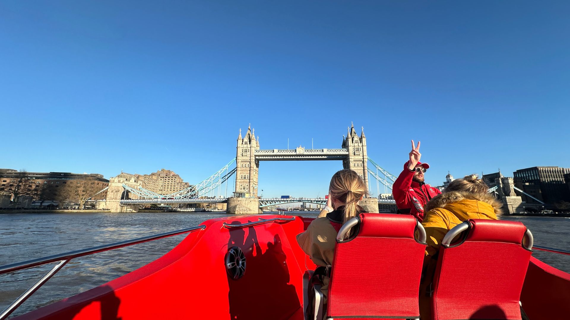 A man wear a red life jacket makes a peace sign in front of tower bridge in london on a red speedboat
