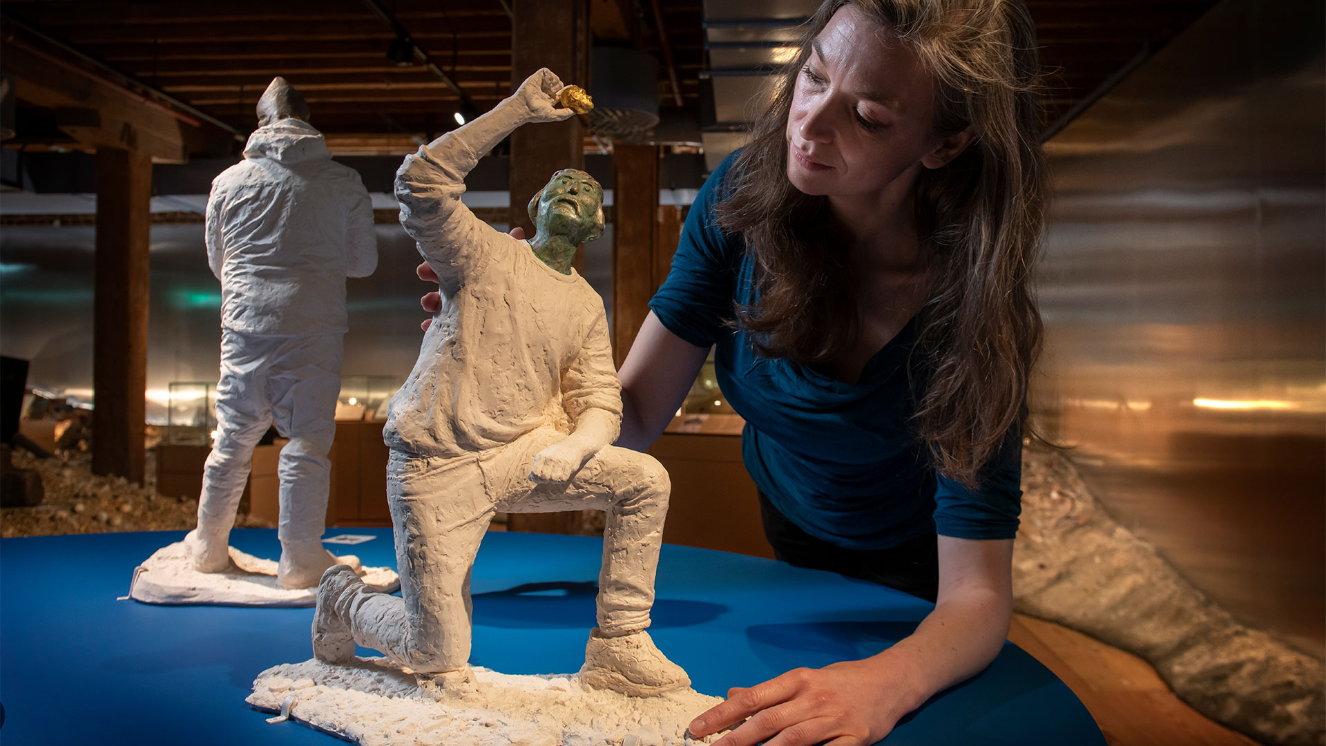 Curator Kate Sumnall stands beside a stone sculpture of a mudlark gazing intently at a golden object discovered in the River Thames.