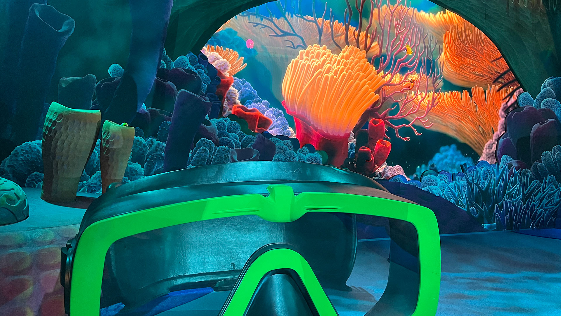 Dive into the underwater world of Finding Nemo at London's new immersive Mundo Pixar exhibition. Photo credit: Carole Rocton. A giant diving mask lies on the ground in the Finding Nemo room at Mundo Pixar, with large coral and submarine life in the background.