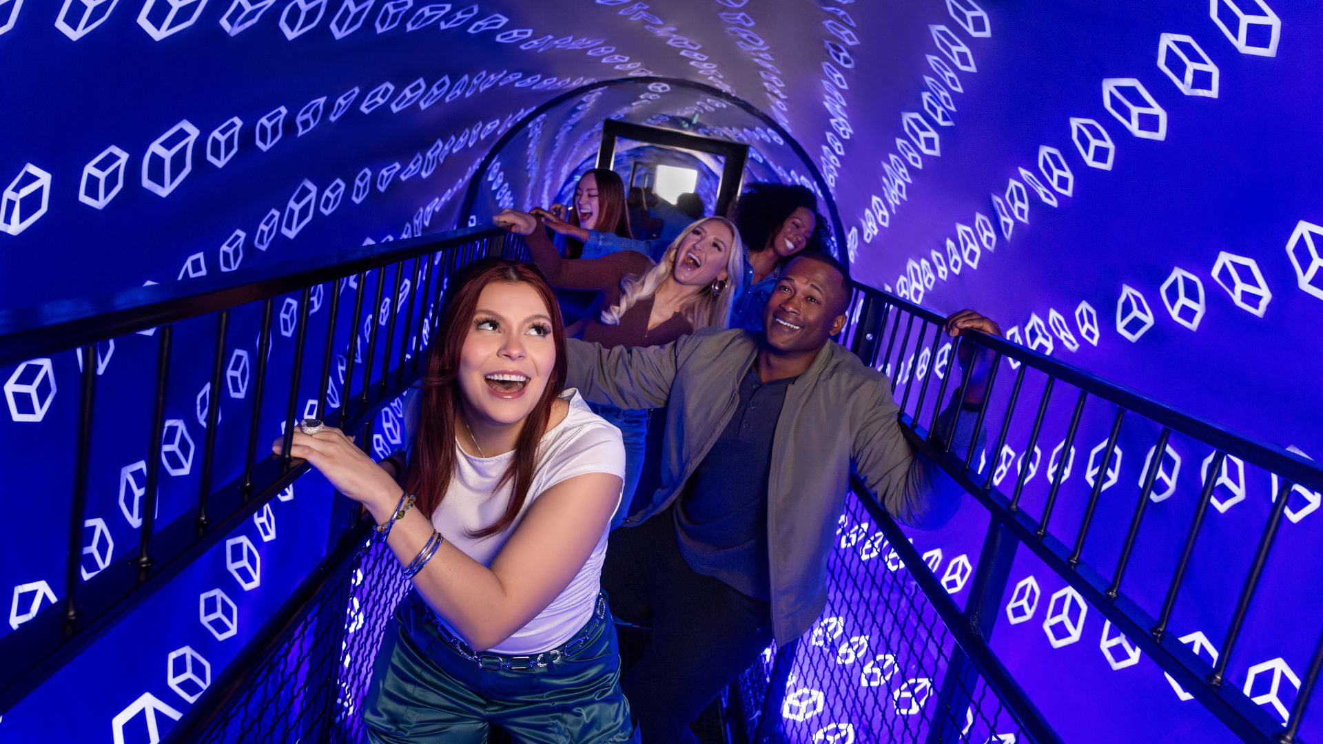 Group of young people in a spinning blue tunnel with black railings.