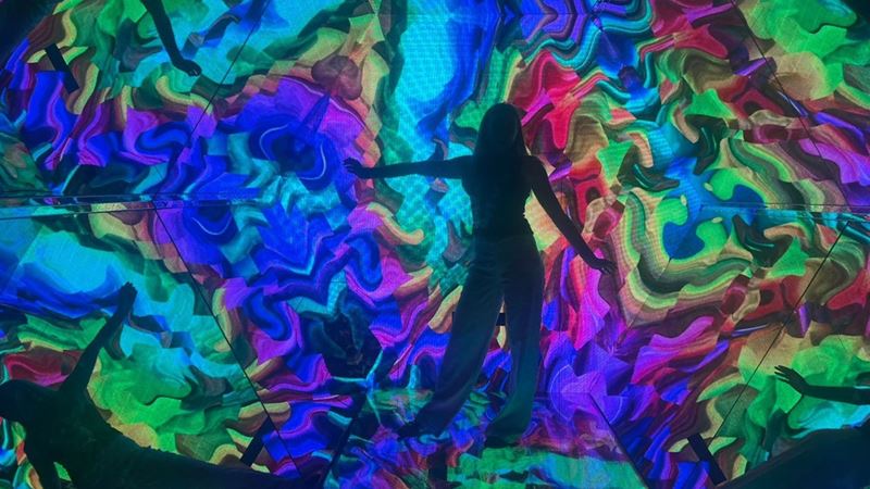 Person standing in a centre of a light tunnel with colourful shapes and reflections all around.