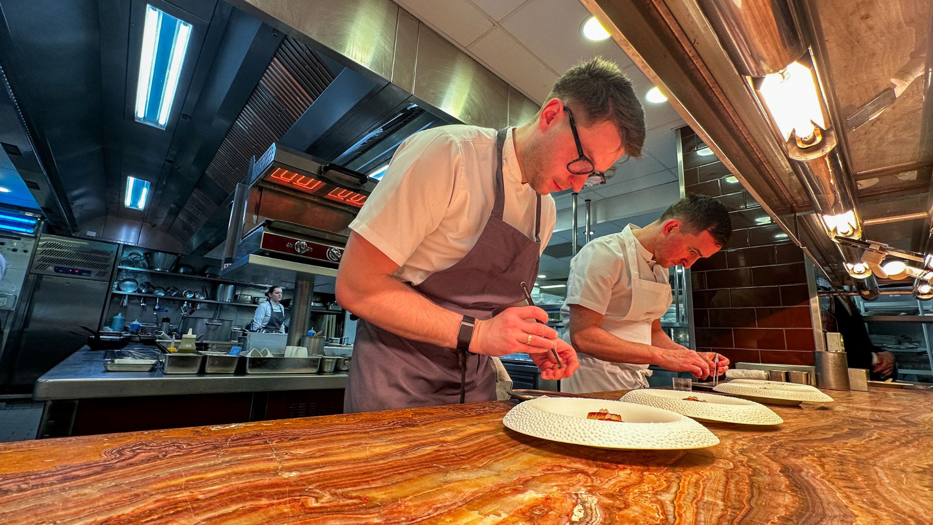 Two chefs carefully plating dishes at the Pétrus kitchen pass under warm lighting.