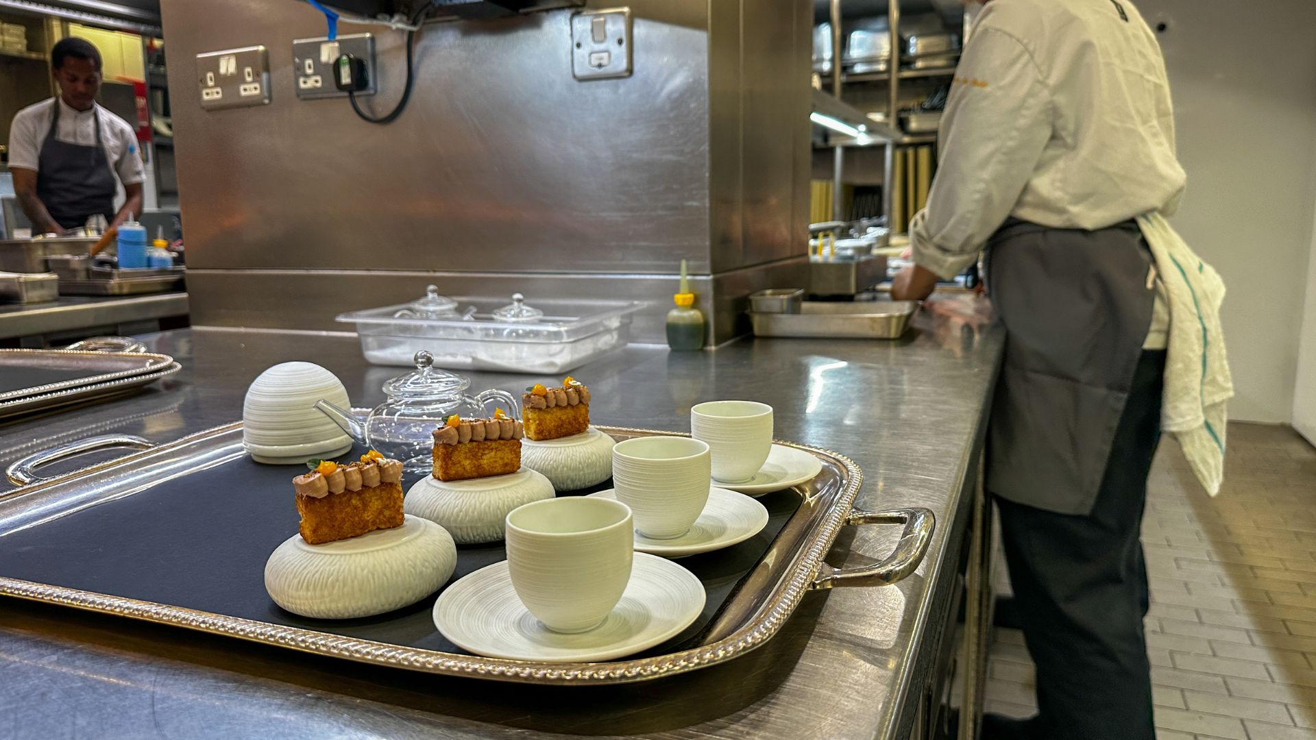 Brioche cakes topped with piped cream served on ceramic stands alongside teacups on a silver tray in the Pétrus kitchen.
