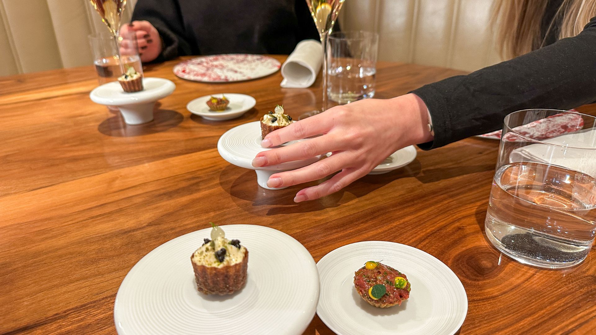 Selection of canapés served on small ceramic stands at the Pétrus Kitchen Table, with a guest reaching for one.