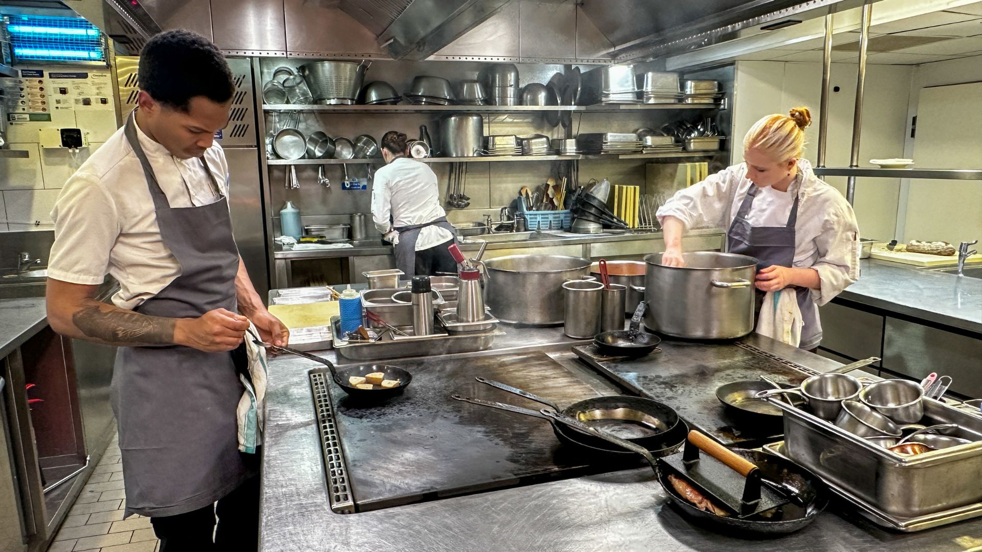 Chefs working over pans and large pots on a stainless steel stove in the Pétrus kitchen during service.