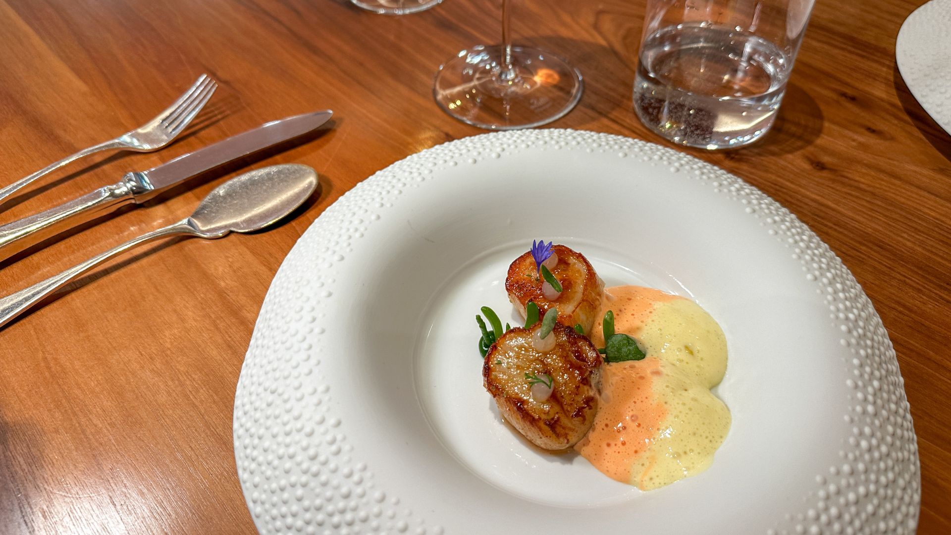 Seared scallop served with golden sauce, mushrooms and micro herbs in a sculptural white bowl at Pétrus London.