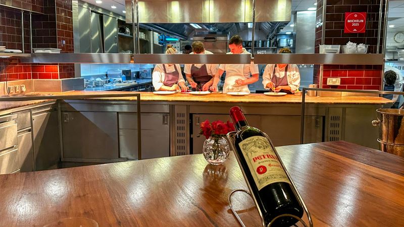 Bottle of Pétrus wine on the Kitchen Table counter with chefs plating dishes on the pass in the background.