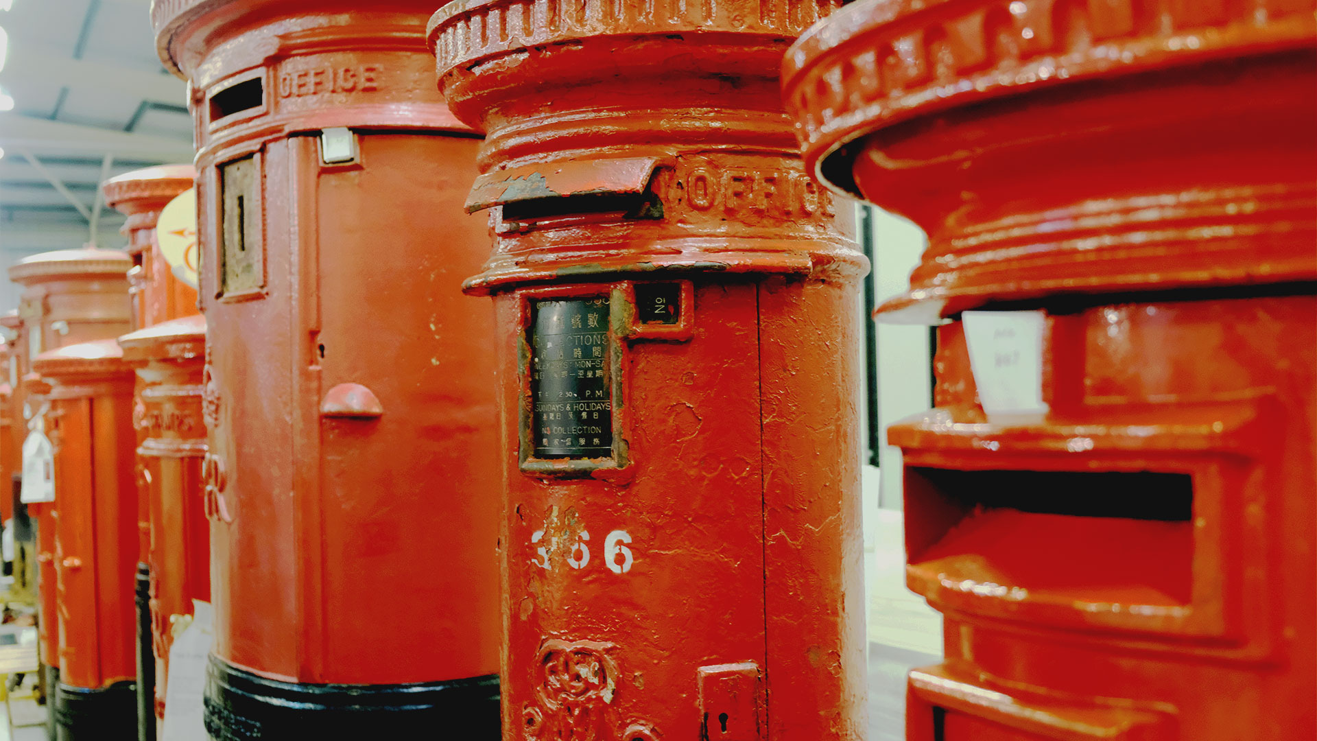 A close-up of a line of red cast-iron post boxes, including a Hong Kong post box with instructions in both English and Chinese.