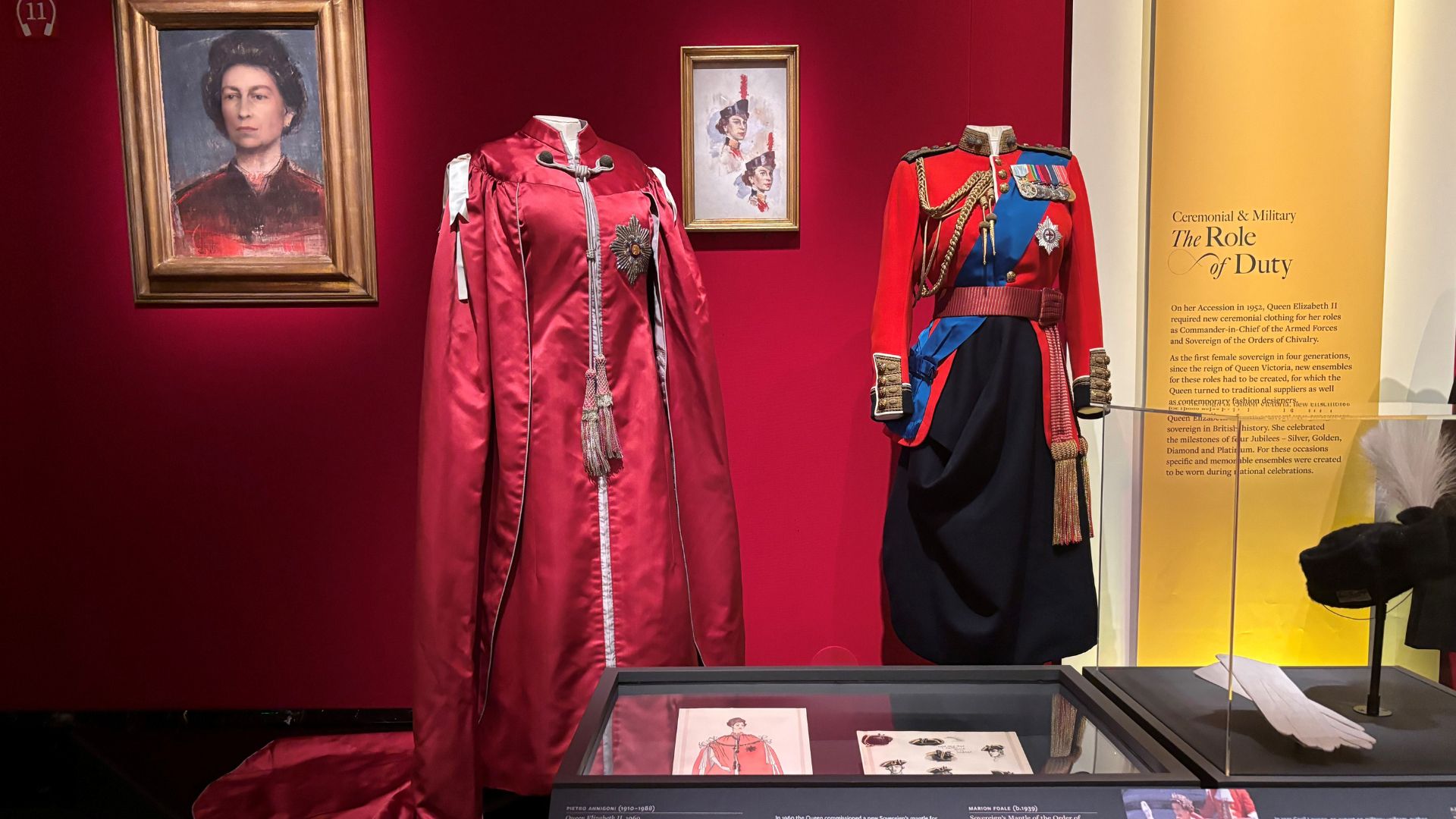 Delve into the stories behind ceremonial clothing at Queen Elizabeth II: Her Life in Style. © Visit London/Charlotte Pritchard. Two items of ceremonial clothing next to each other with portrait of the Queen beside them at Queen Elizabeth II: Her Life in Style.