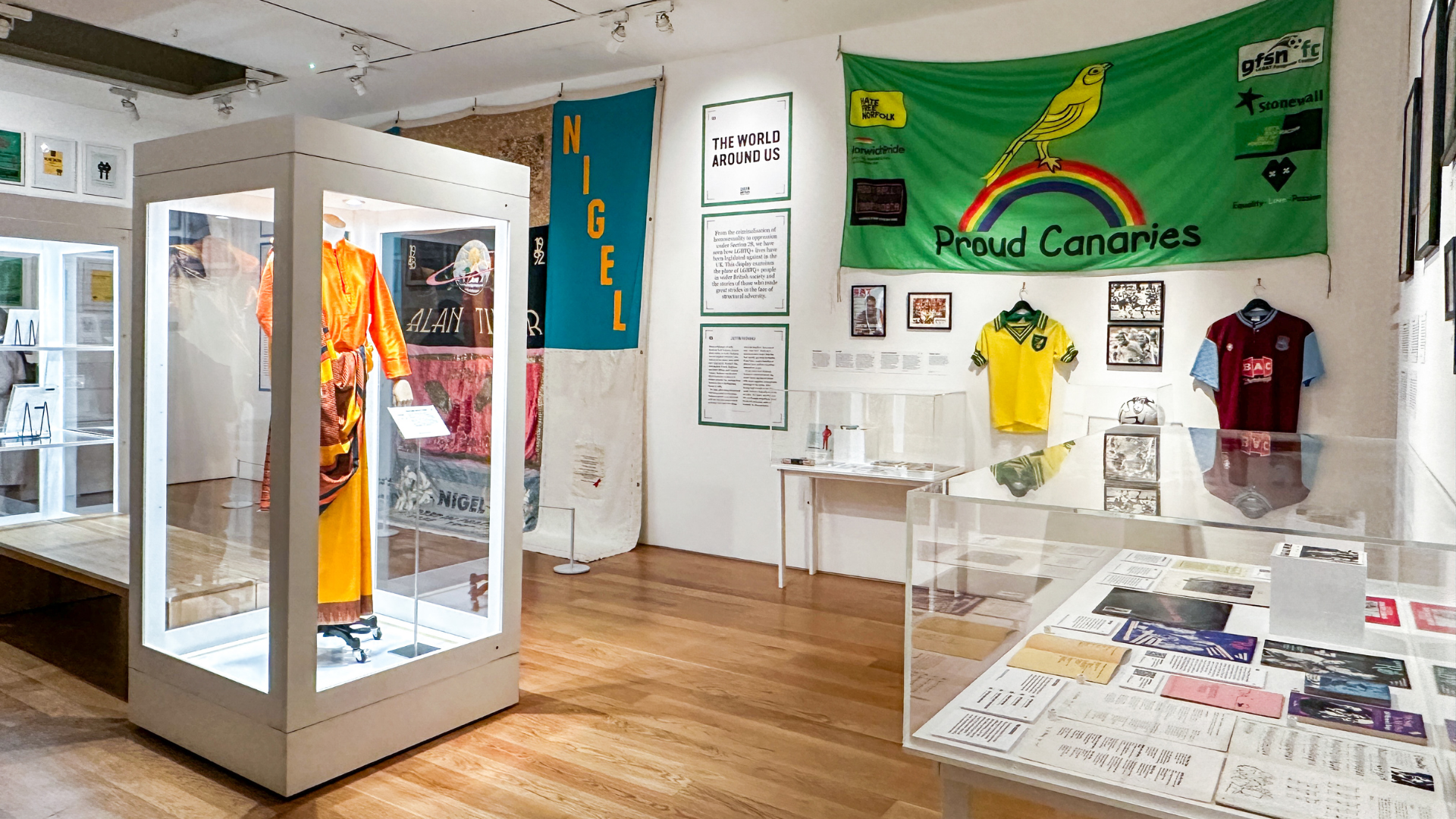 A wider view of Queer Britain’s thematic galleries, bringing together fashion, sport, protest and community through objects, banners and archival documents. Image credit: Visit London/Kirstine Spicer A museum gallery with display cases, banners and framed artefacts exploring different themes in LGBTQ+ history, including sport and activism.