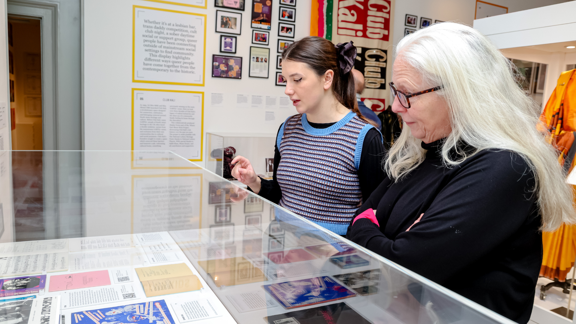 Visitors explore Queer Britain’s exhibitions together, engaging with archival documents, personal stories and moments from LGBTQ+ history.Image courtesy of Queer Britain. Photo credit: Rahil Ahmad. Two visitors stand side by side reading text and archival materials inside a glass display case at Queer Britain Museum.