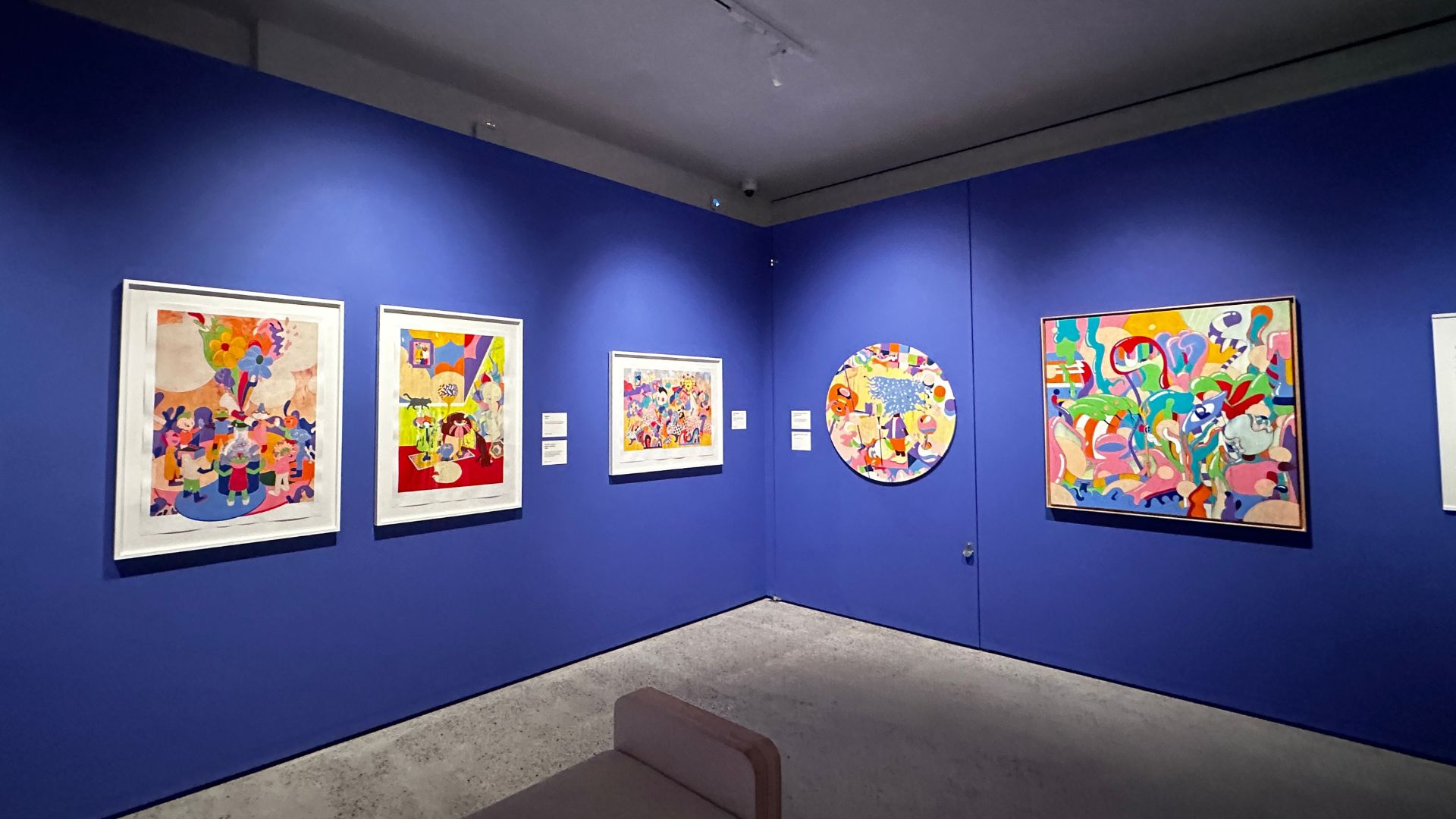 MURUGIAH draws on personal experiences, cultural influences and contemporary design to create artwork that is both joyful and deeply reflective. Photo Credit: Kirstine Spicer/Visit London. Colourful artworks by MURUGIAH displayed in a gallery space alongside exhibition interpretation panels.