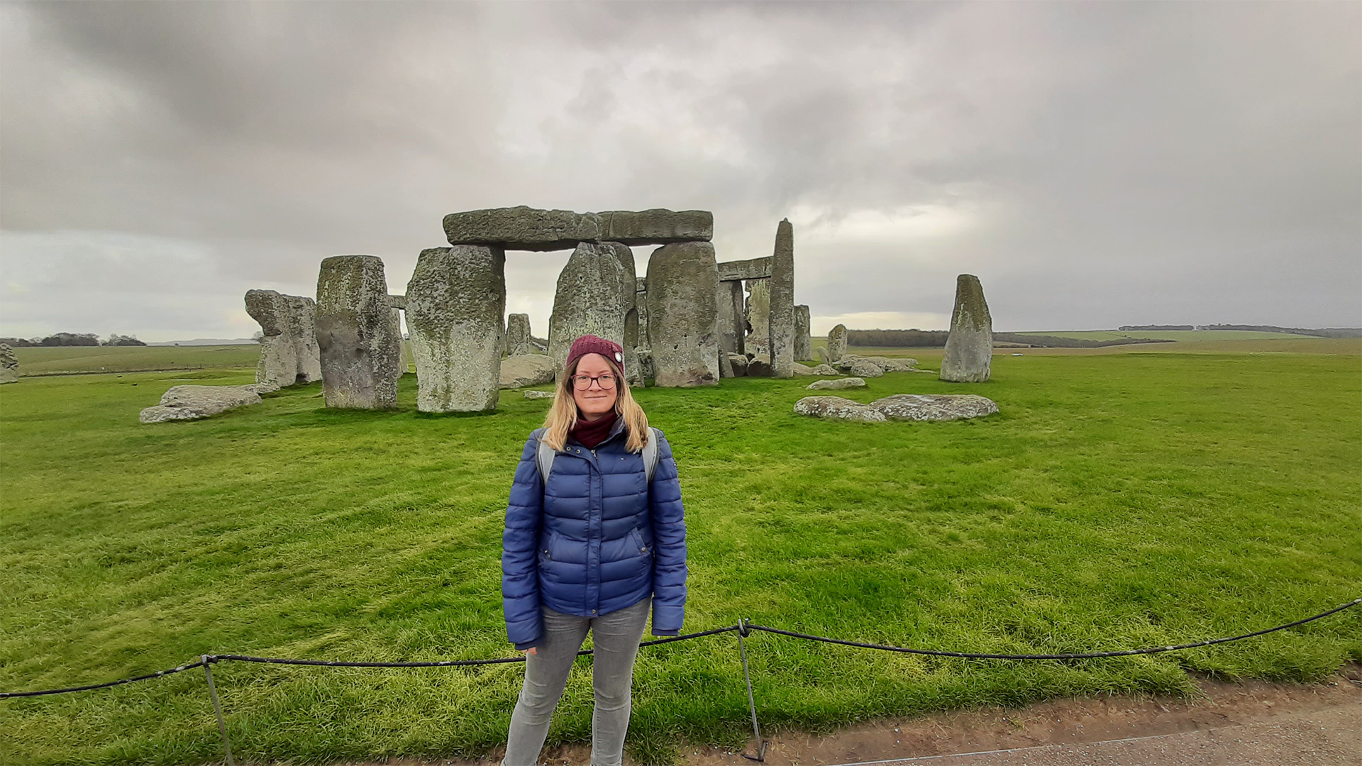 A women in winter clothing stand in front of Stonehenge.