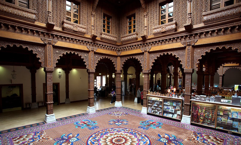 The Haveli at BAPS Shri Swaminarayan Mandir. Image courtesy of BAPS Shri Swaminarayan Mandir. The Haveli inside BAPS Shri Swaminarayan Mandir with ornate tiled flooring and carved wooden walls with arches and columns.