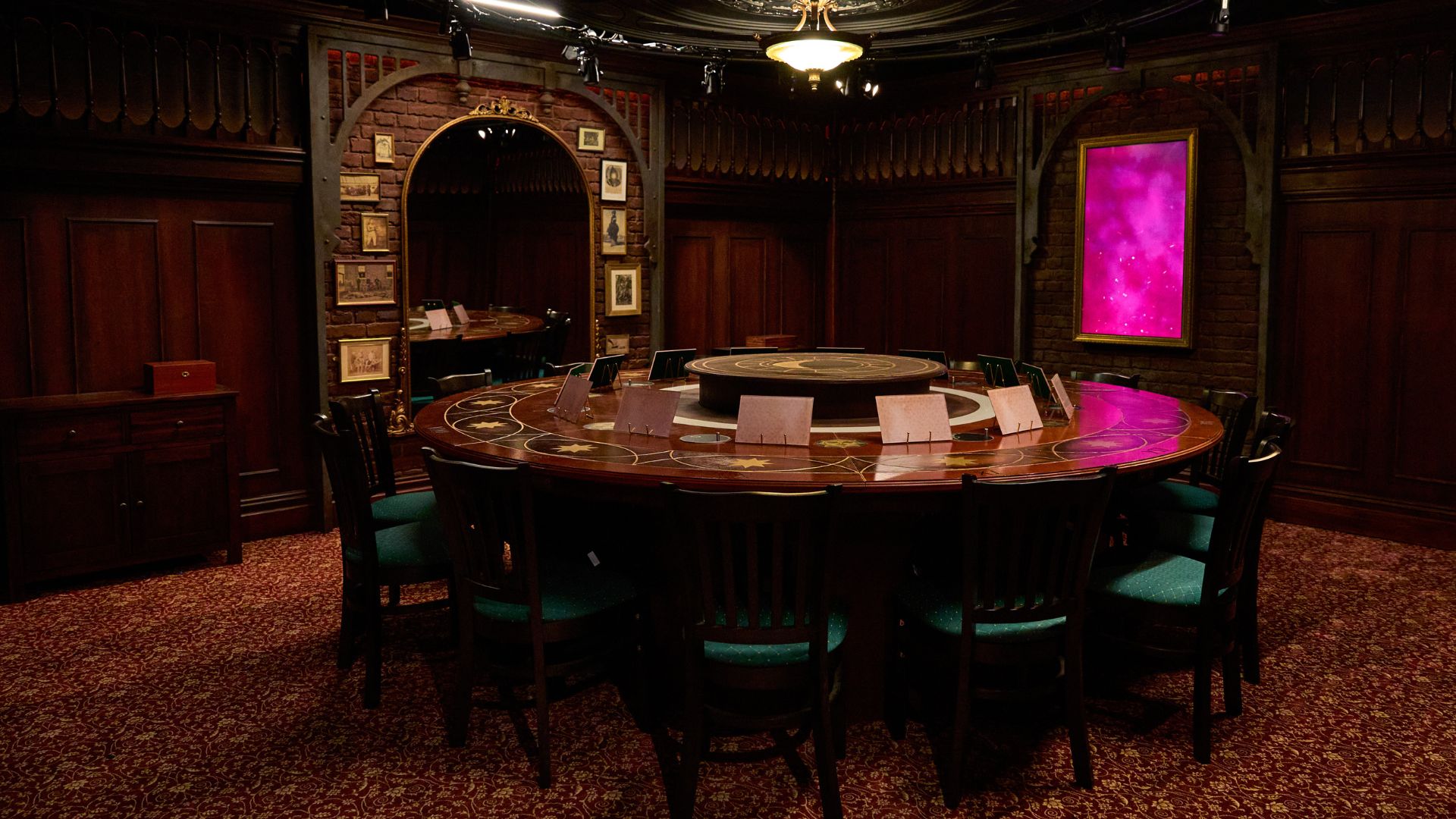 Step into the world of the hit TV series at The Traitors: Live Experience. Image courtesy of Mance Communications. Photo credit: Hugo Glendinning. Round table with whiteboards lined next to each other and interactive screen in background.