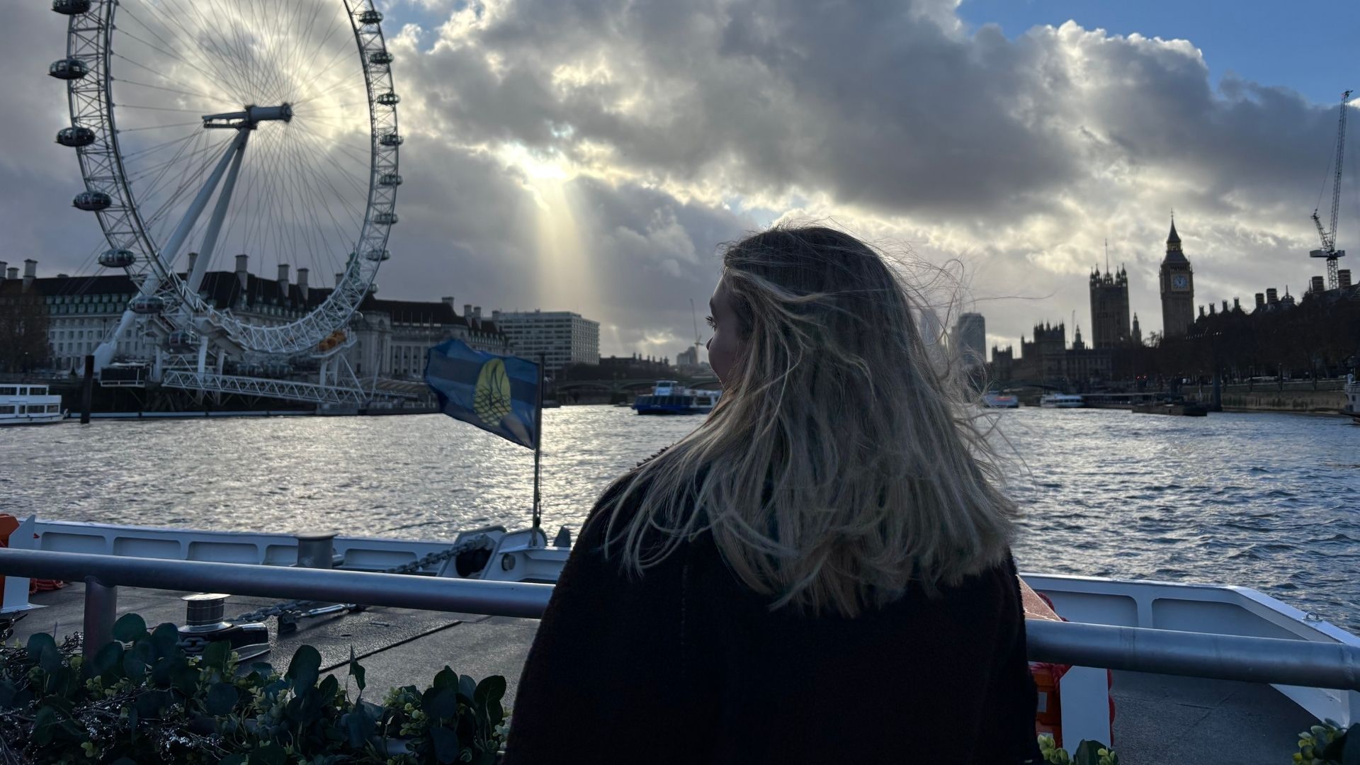Person looking out over the open-air deck of a river cruise with views of the London Eye.