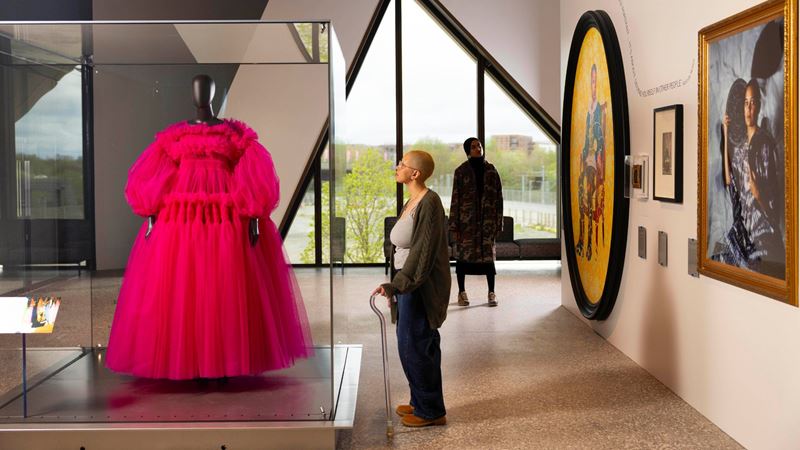 Bright pink Molly Goddard Daria dress with artworks surrounding it and person looking up at cabinet.