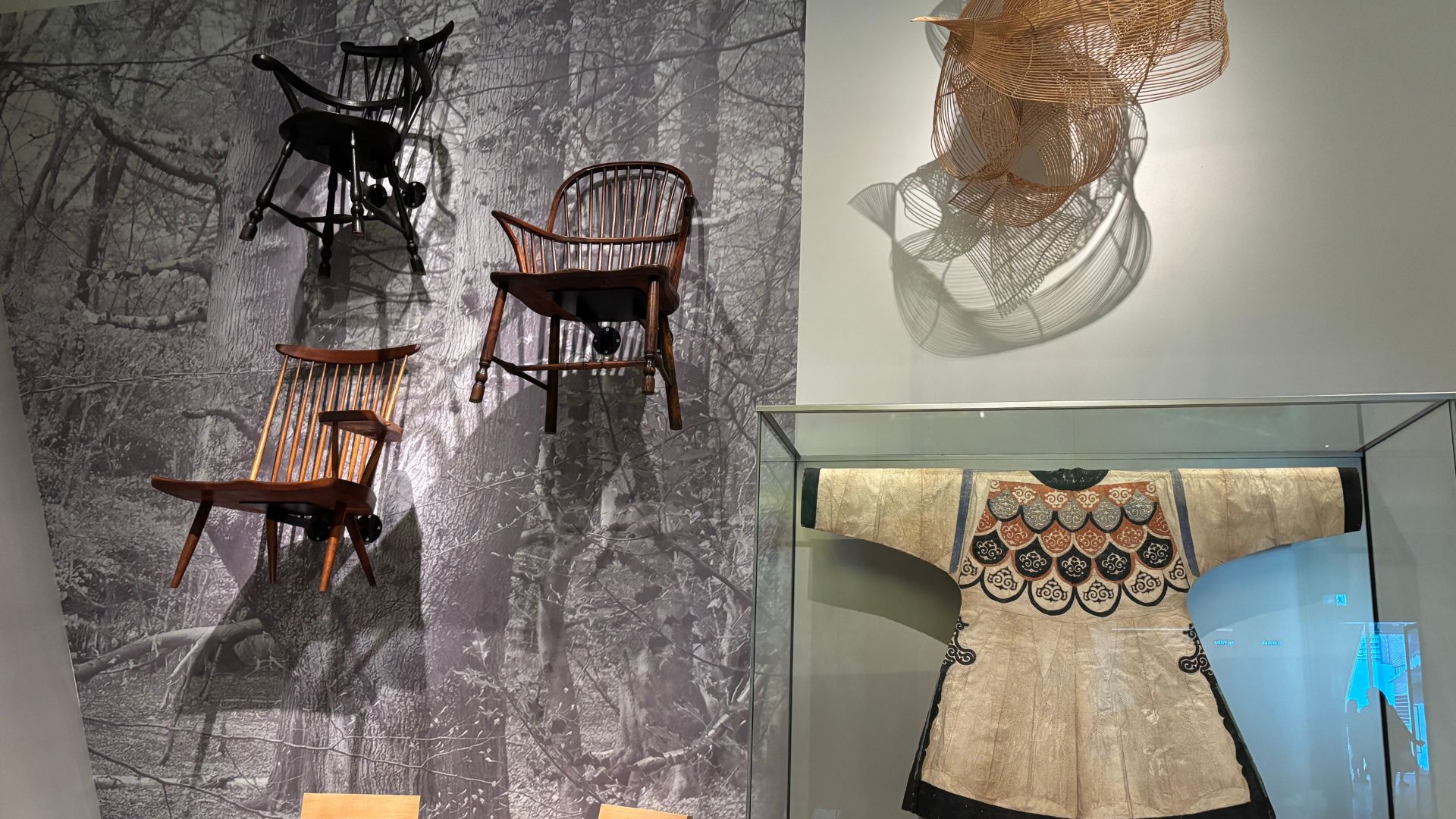 See fascinating objects representing stories from around the world at V&A East Museum. © Visit London/Charlotte Pritchard. Wooden chairs hanging on wall alongside tapestry and textural objects at V&A East Museum.