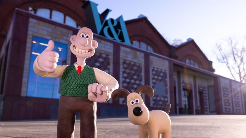 Wallace & Gromit outside Young V&A. Photo by David Parry for the V&A. Wallace and Gromit clay figures posed outside Young V&A, with Wallace giving a thumbs-up and the museum’s distinctive signage visible above the entrance.