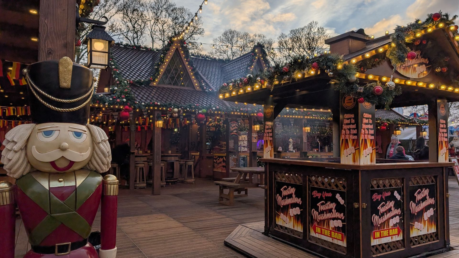 Festive Christmas market stalls decorated with garlands and lights, featuring a large wooden nutcracker figure in the foreground.