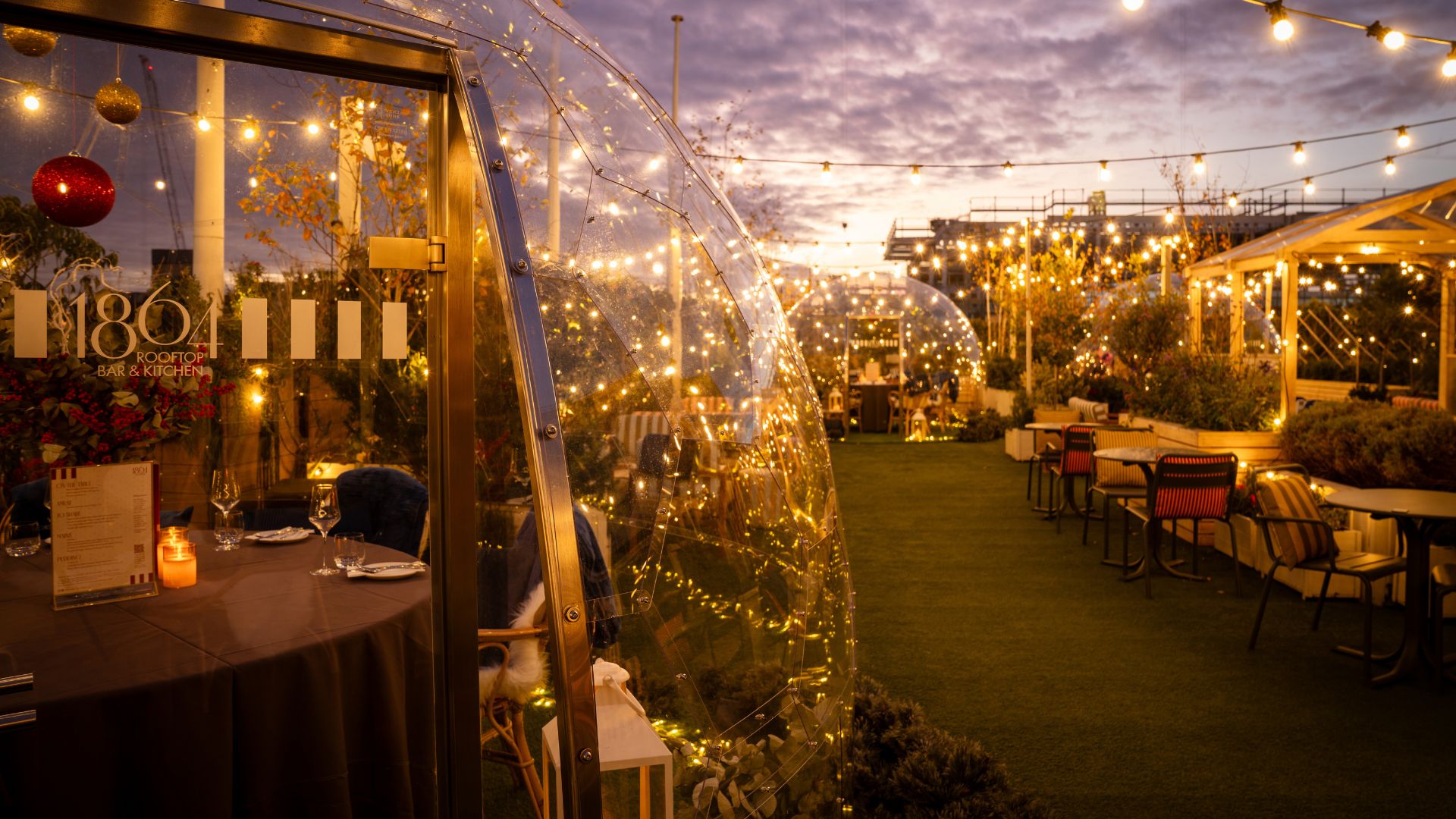 Dining igloos lining a rooftop with fairy lights above.