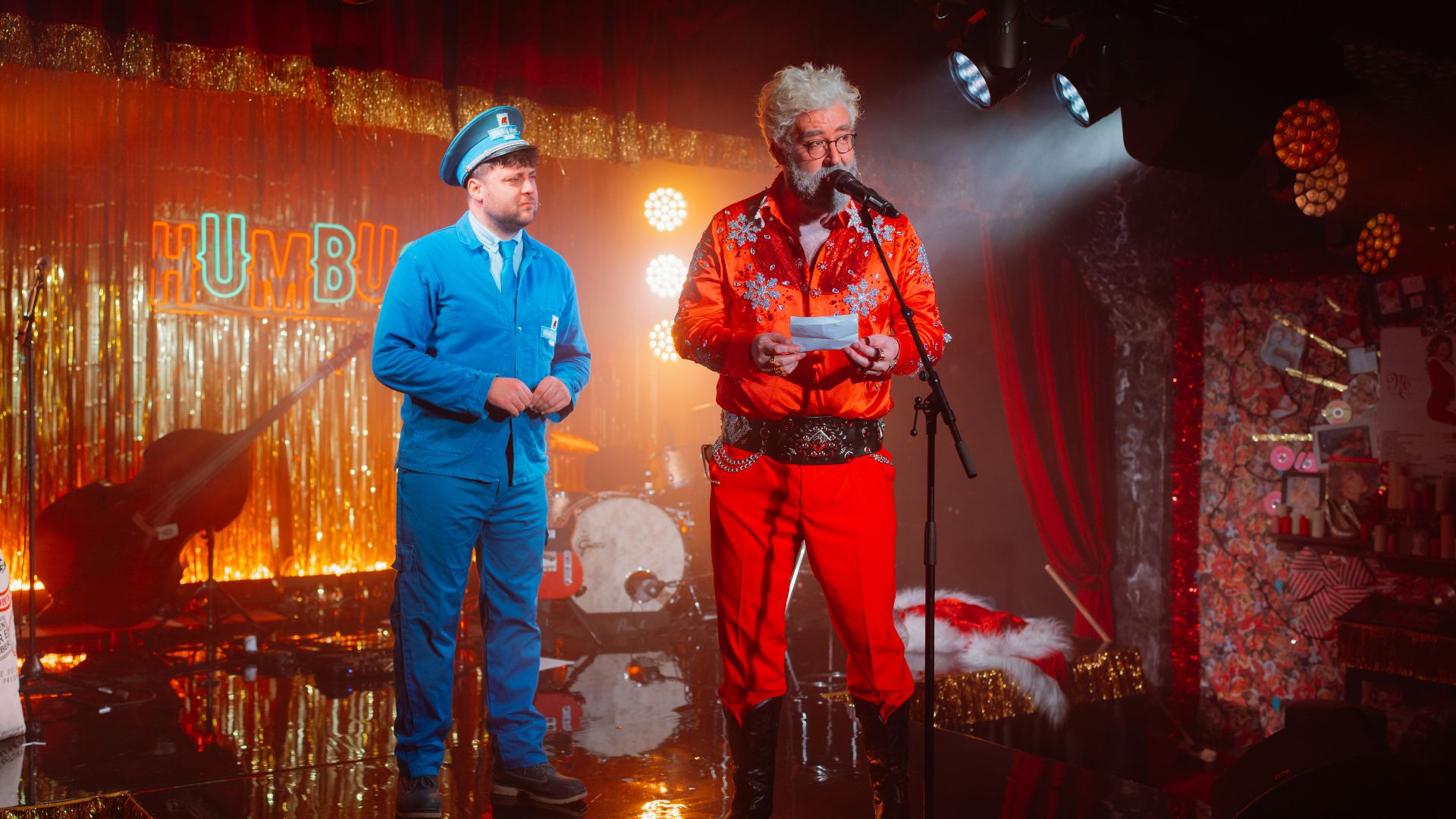 HUMBUG: Santa’s Christmas Dive Bar Experience. Photo credit: Grant Walker. Image courtesy of Mance Communications. Actor dressed as Santa Claus and another person dressed as a mailman on stage with a Humbug sign in the background.