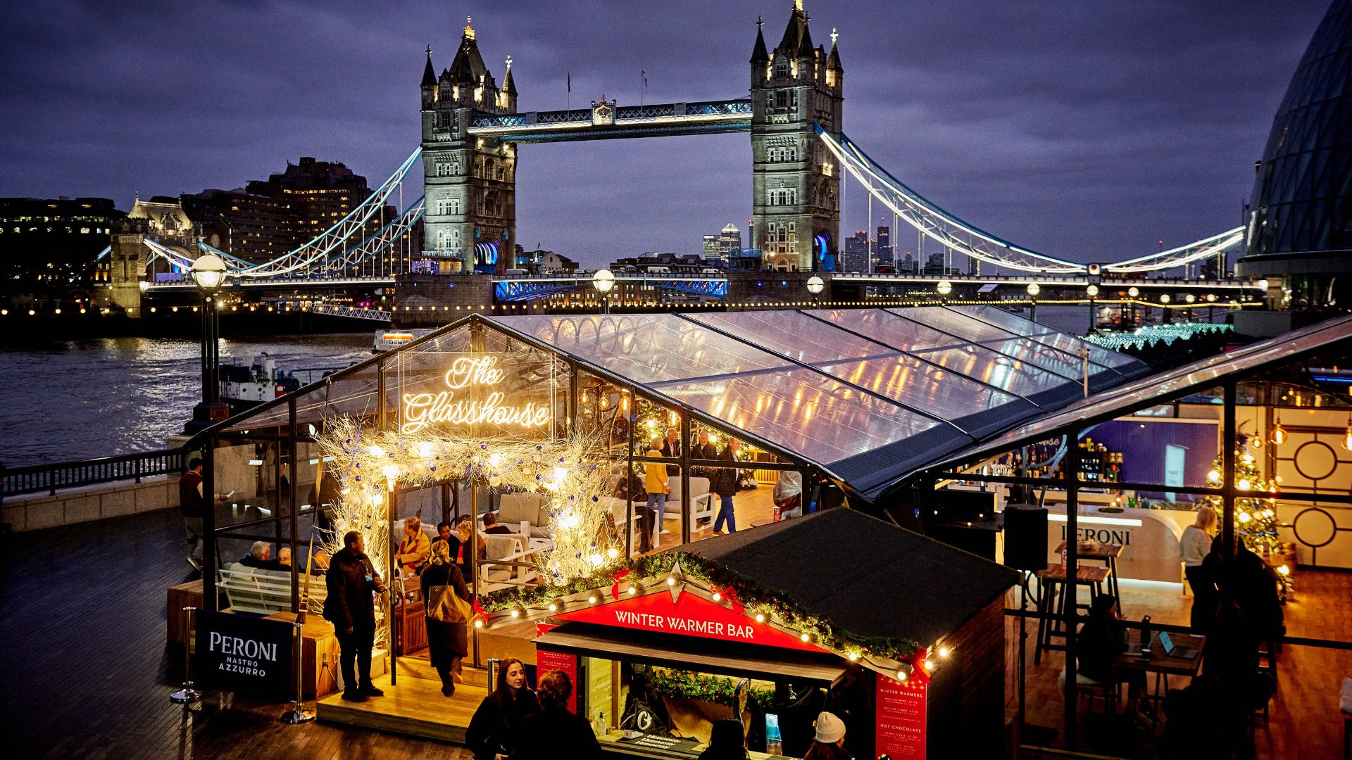 Winter by the River 2024. Photo credit: Dennis Davis. Image courtesy of Axe and Saw. Winter by the River's glasshouse with Tower Bridge in the background.