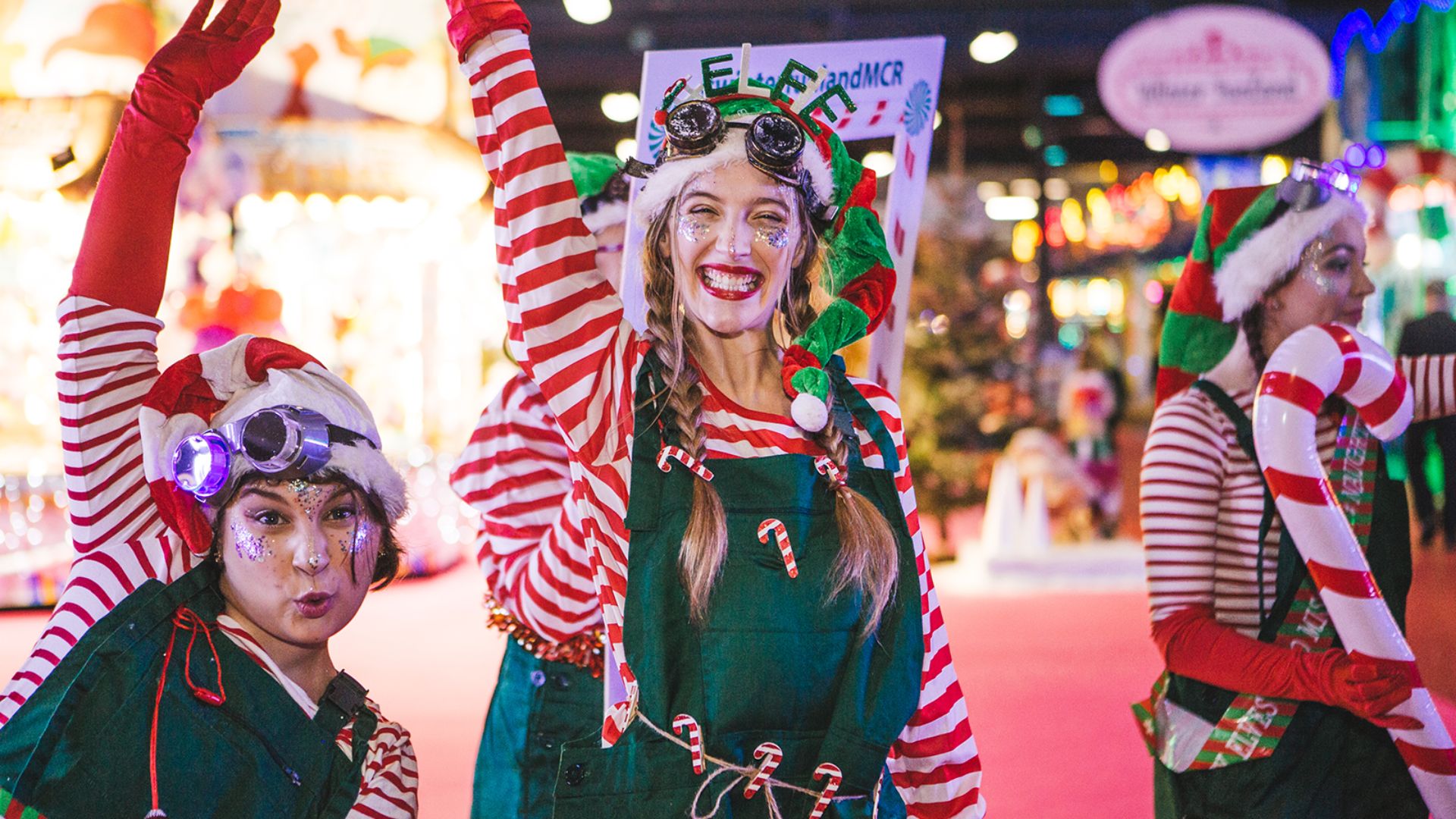 Winter Funland at Olympia. Image courtesy of Olympia London. People dressed up as Christmas elves with one holding a candy cane.