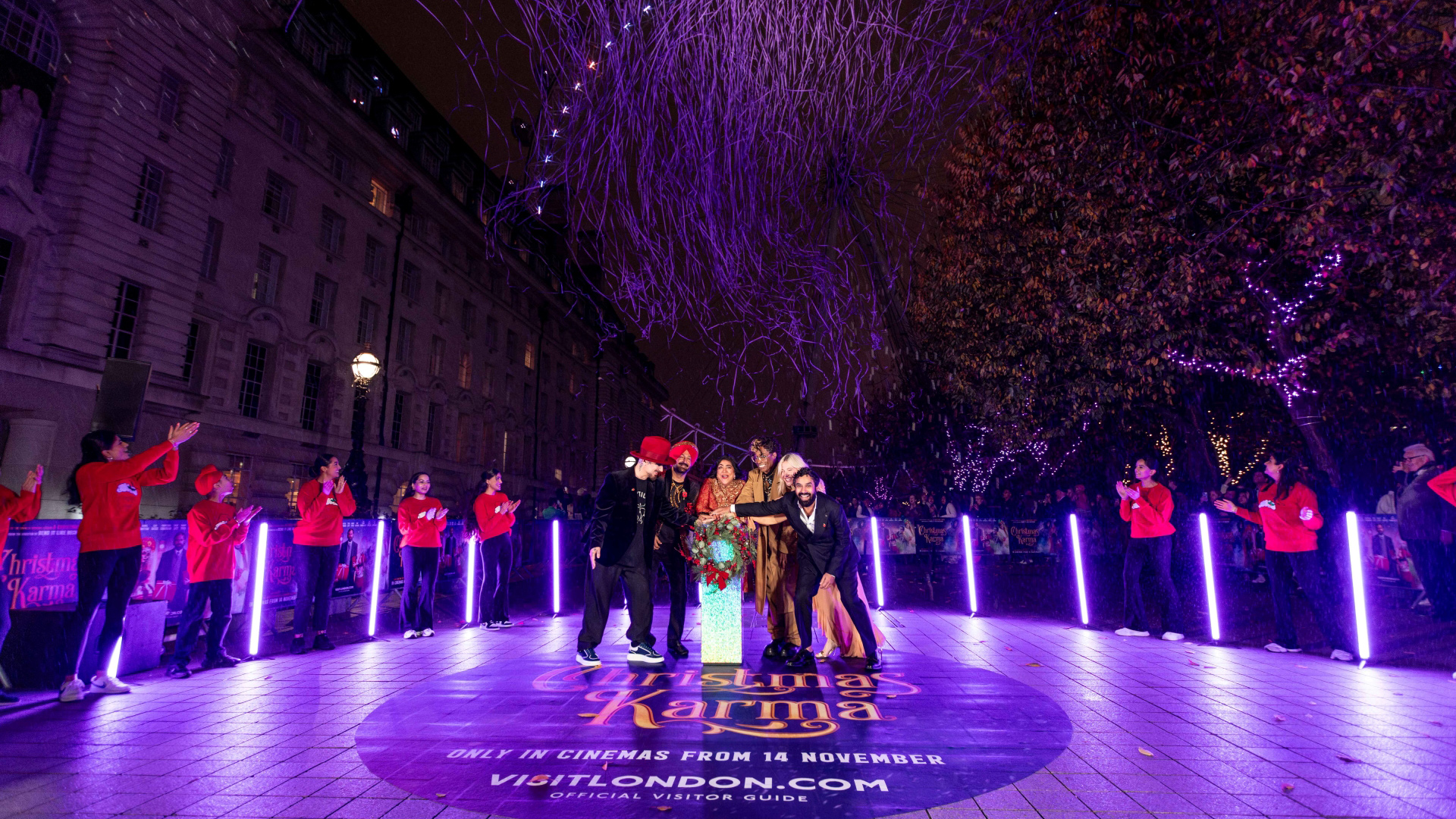 A photo of the cast of Christmas Karma at the London Eye Christmas light switch on with the logo on a giant sticker on the floor with visitlondon.com below with the London Eye in the background