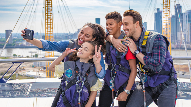 Une famille souriante prend un selfie avec la ville en arrière-plan au sommet d'Up at the O2.