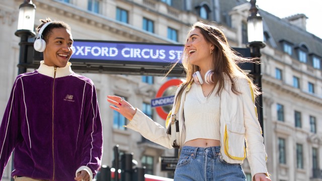 Deux personnes se sourient et rient devant une station de métro sur Oxford Street.
