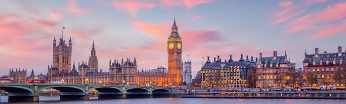 London skyline at sunset with pink and blue sky, viewed from the river Thames, featuring Big Ben and the Houses of Parliament.