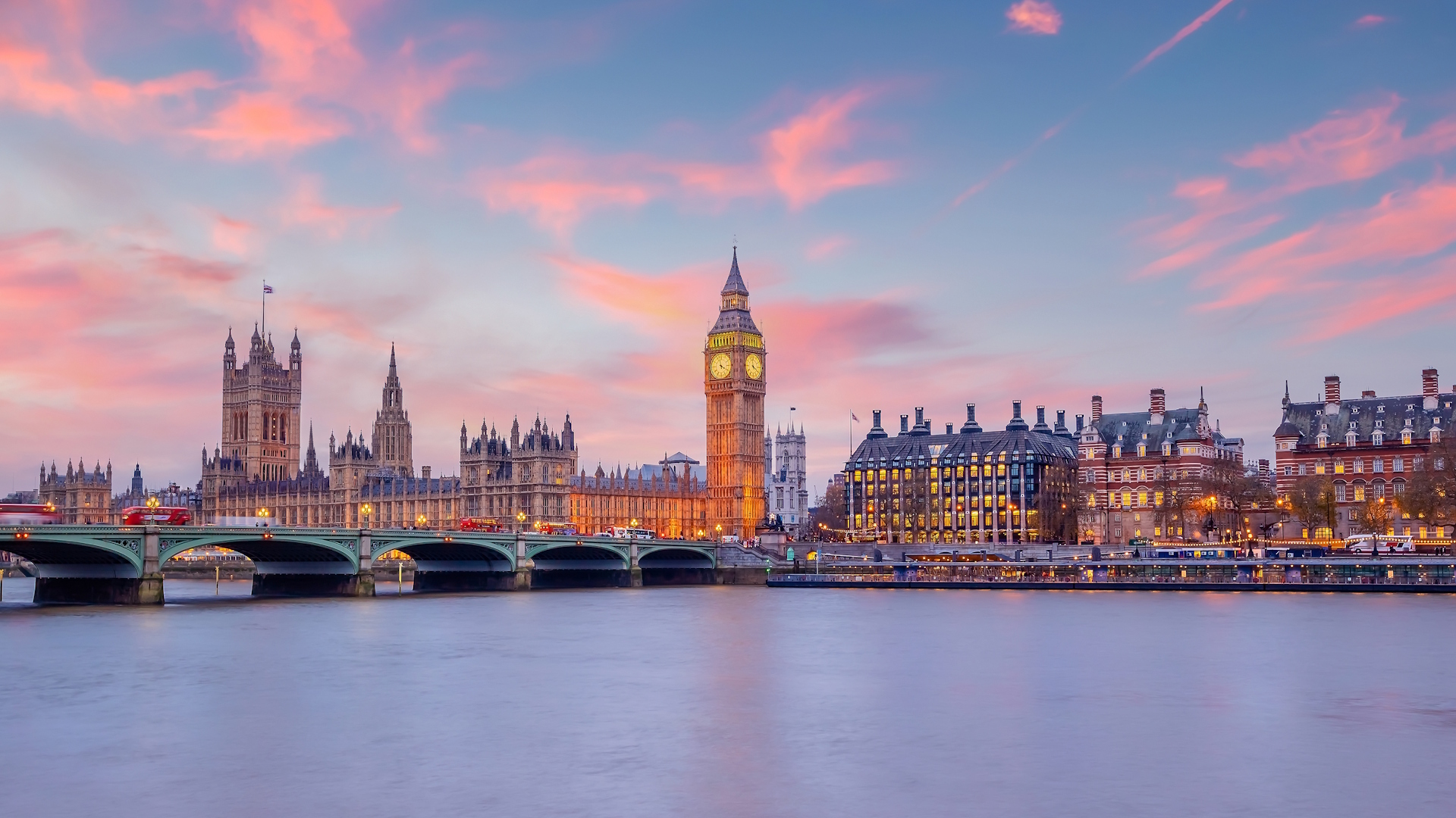 London skyline at sunset with pink and blue sky, viewed from the river Thames, featuring Big Ben and the Houses of Parliament.