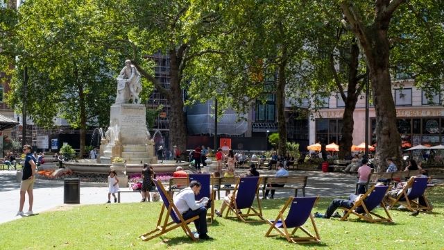 People sit in chairs around a statue at London's Leicester Square gardens.