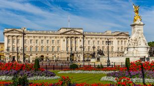 Buckingham Palace on a sunny day with red and purple flowers in bloom in the memorial gardens.