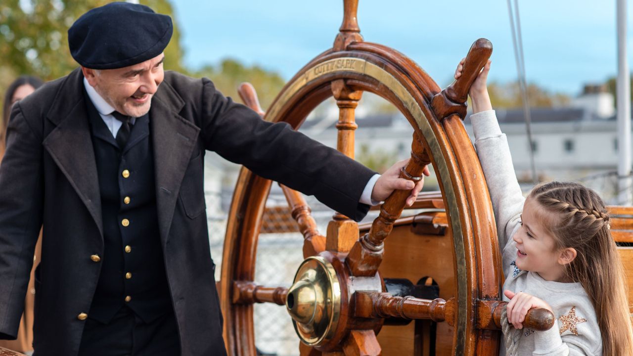 A young girl steers the wheel of the Cutty Sark ship in Greenwich London.