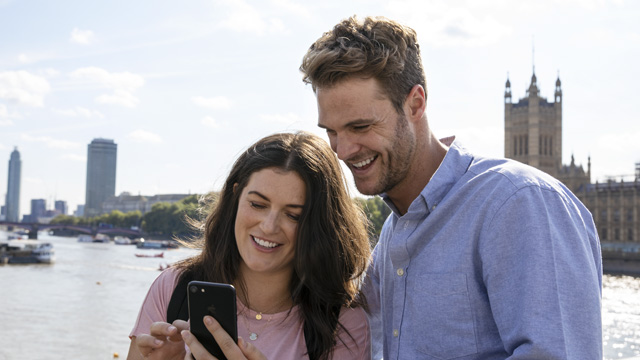Un couple se tient près de la Tamise sur Londres et consultent une liste d'attractions disponibles sur l'application du London Pass.