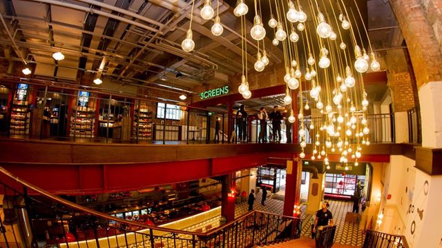 The interior of Picturehouse Central in London, featuring a grand staircase, cinema screens and decorative hanging lights.