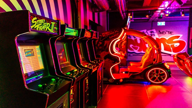 Retro arcade games at Queens. Image courtesy of Queens. A vibrant room with neon decor and arcade machines and games