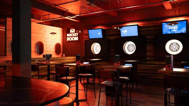 Interior of an activity bar, featuring interactive darts lanes, tables and ambient lighting.